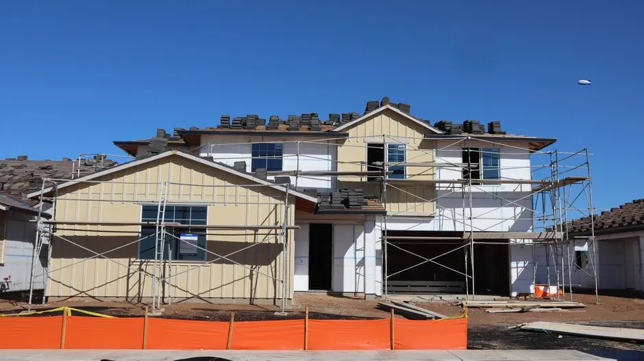 Modern two-story house under construction with visible scaffolding and building materials.